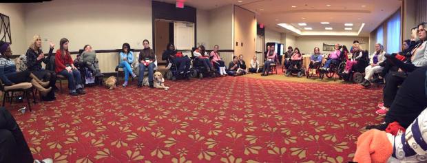 Photo of a wide view of a large meeting space with people with disabilities in a large circle.