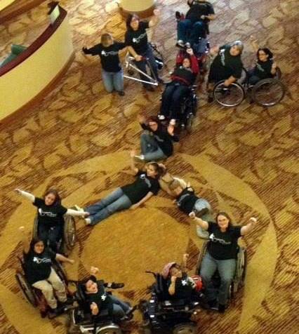 View looking down from a second floor of girls with disabilities, including some in wheelchairs gathered together forming the shape of the symbol for women