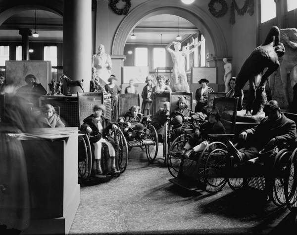 Black and white photo of a group of students in large wheelchairs at the Metropolitan Museum of Art on November 23, 1922
