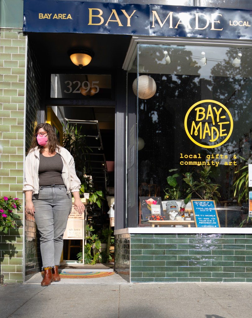 Professional illustrator and Bay-Made business-owner Sarahjane Bernhisel models a bright pink KN95 mask as she stands in the entrance of her store. Photo by Brian Ringo, 2023.