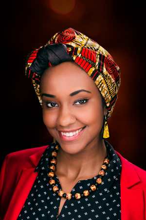 Image description by Azza: Azza, a Black woman, wears a bright red and gold hijab with an East African print, red blazer, and black button down blouse. She is smiling at the camera.