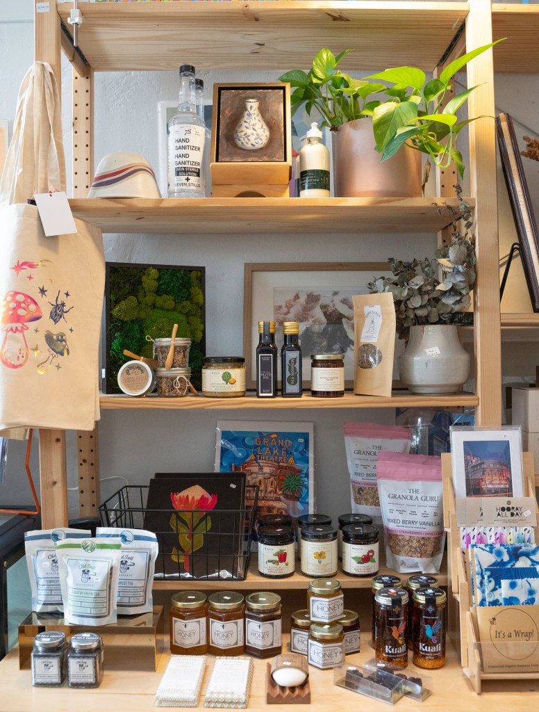 Display shelves with various items, including houseplants, art, a mushroom bag, cooking oils, honey, tea, soap, and more. Photo by Brian Ringo, 2023, used with permission.