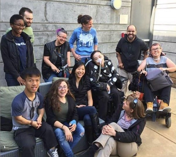 Photo from a gathering of disabled friends I hosted at my home several years ago with Stacey on the right side of the image. Everyone is smiling and laughing.