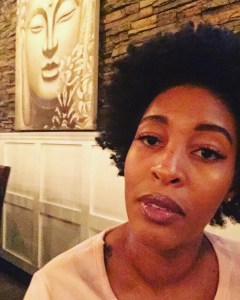 Image description: Woman with an afro sitting to the right of a large picture of Buddha.