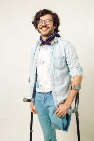 Alex, an above the knee amputee, poses joyously in a monochromatic light blue outfit and a dark blue bandana around his neck. Balancing on his crutches, he beams looking off into the distance with his dark brown, wavy hair framing his face.