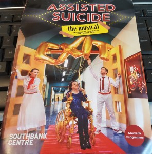 Program from the theatre show, "Assisted Suicide: The Musical" featuring a white woman sitting in a gold wheelchair. On both sides are two people dressed in white and red guiding her down a red carpet. These people are holding helium balloons with spelling the word, "Exit"