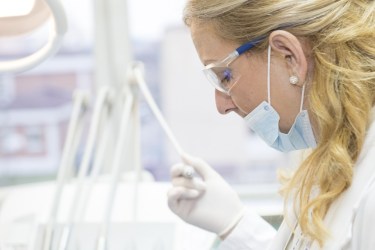Image of a white female doctor with blonde hair. She is wearing a mask over her mouth, latex gloves and a lab coat