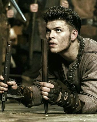 Image description: screenshot from an episode of Vikings, an original series on the History Channel. Ivar the Boneless is a young Viking warrior with short dark hair. He is on the floor in a crawling position. He is looking upward. In both of his hands he is holding sharp wooden sticks to help pull his body forward when crawling.