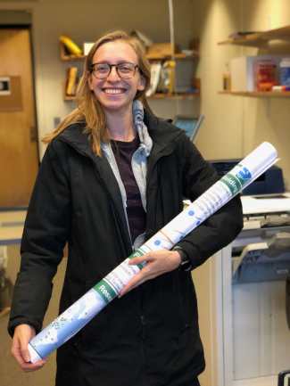 Gabi smiling and holding a large poster in an office.