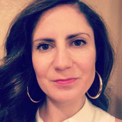 Conchita Hernandez Legoretta, a Latina woman smiling at the camera. She has long wavy brown hair and is wearing gold hoop earrings.