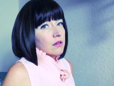 White woman wearing high-collared shirt looks at camera. No smile.