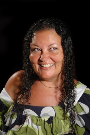 Image of Patty Berne, a Japanese-Haitian queer disabled woman.  She has long curly dark hair and is smiling widely and looking to the right of the camera. She is wearing an off-the shoulder shirt in a white, navy, and green pattern. Image credit Richard Downing courtesy of Sins Invalid.