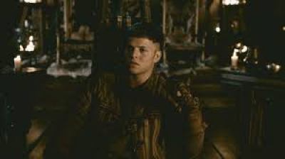 Image description: screenshot from an episode of Vikings, an original series on the History Channel. Ivar the Boneless is a young Viking warrior and he is sitting alone in the Great Hall of Kattegat, the home of Ivar and his family. He looks like he is contemplating something.