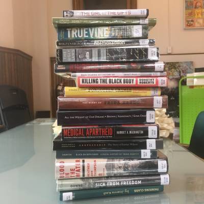 A stack of 17 library books lying horizontally. Text on the spines of the books from top to bottom: The Girl with All the Gifts, Disability and Difference in Global Contexts, Truevine, Normalization, The Ugly Laws, Kindred, Black Disabled Art History 101, Killing the Black Body, Forgotten Crimes, The Diary of Frida Kahlo, All the Weight of Our Dreams, Medical Apartheid, Unspeakable: The Story of Junnius Wilson, Black on Both Sides: A Racial History of Trans Identity, Blood in the Water, Sick from Freedom, Thinking Class