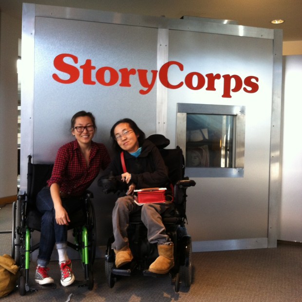 Two Asian American women in wheelchairs sitting in front of a StoryCorps recording booth