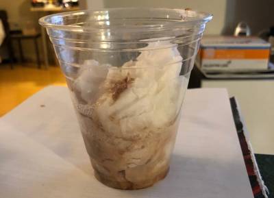 A clear plastic cup filled with tissues soaked with saliva with streaks of brown from something chocolatey.