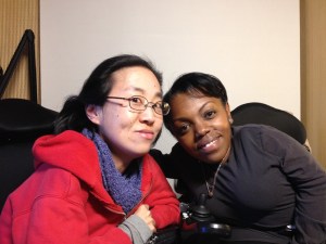 Image of two women in wheelchairs. On the left is an Asian woman with glasses and wearing a red hoodie. On the right is an African American woman with short black hair and a black shirt.