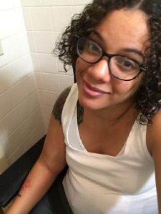 Image description: Jess has a medium light complexion, dark curly hair, is wearing glasses, and smiling sideways into the camera.