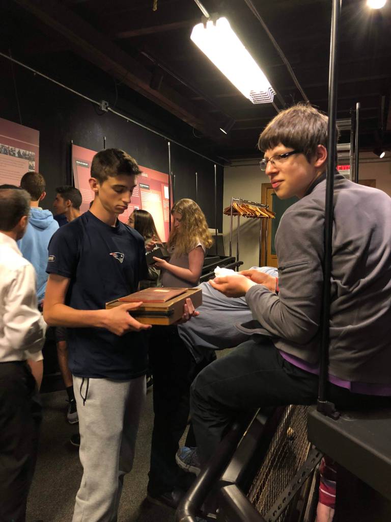 Student Teddy Bennett stands at left in front of an exhibit case holding an early IQ test alongside student Zachary Sherman, putting together a museum exhibit on disability history. Photo courtesy of Gann Academy. Photo credit: Maya Wainhaus