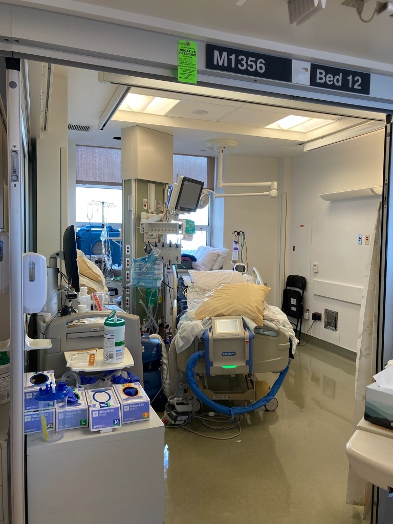 Adios, 13th floor, Moffitt Hospital! I was in multiple rooms on the 13th and 9th floor ICU units for 4 weeks but this was my final location, M1356, Bed 12. There is a hospital table and many drawers and containers of supplies such as latex gloves and disinfectant wipes. Equipment and tubing is in the center of the room, adjacent to the bed.
