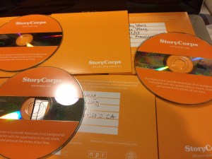 Image of several orange envelopes with the word StoryCorps and CDs arranged in a row.