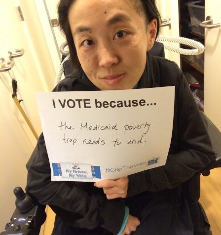 Photo of an Asian American woman in a wheelchair holding a white piece of paper that says, "I Vote because...the Medicaid poverty trap needs to end."