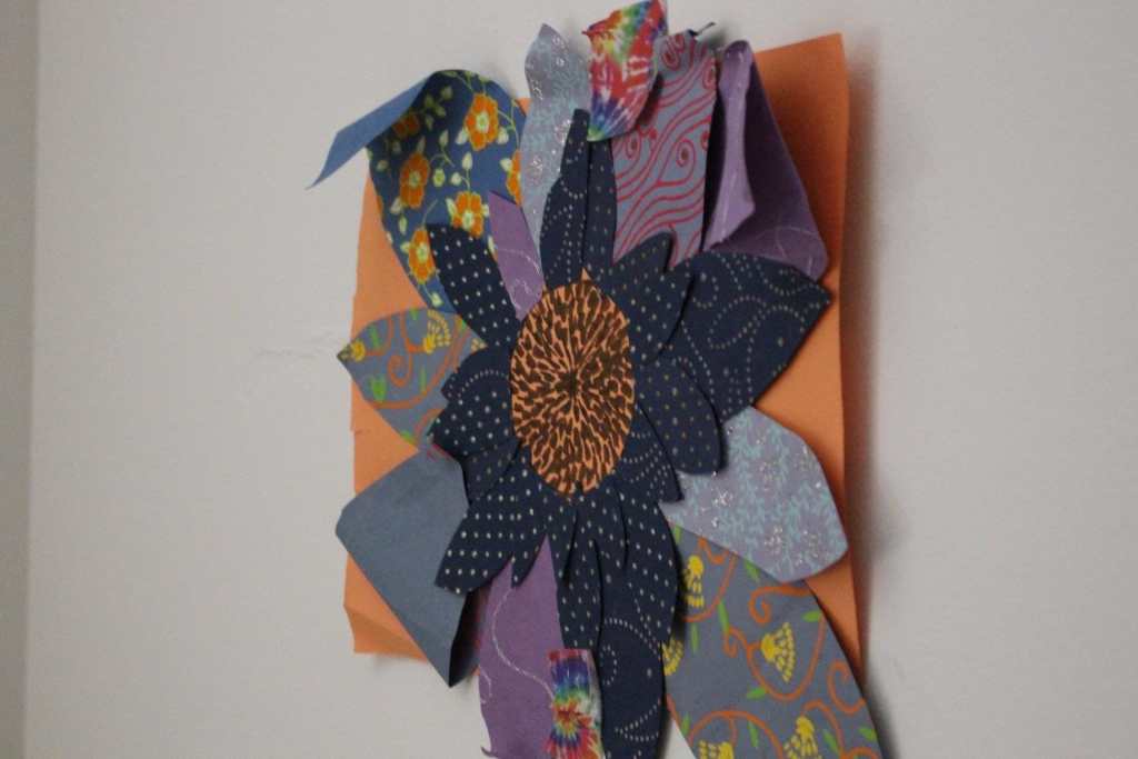 [A flower made up of multiple kinds and colors of fabric on orange paper]