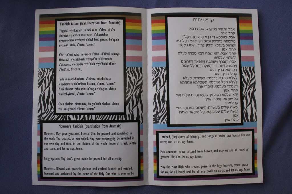 [The inside of Emet’s funeral program. Kaddish Yatom and its transliterations are on either side The bottom has the Mourner’s Kaddish translation into English The background is rainbow pride flags, trans pride flags, and zebra stripes.]