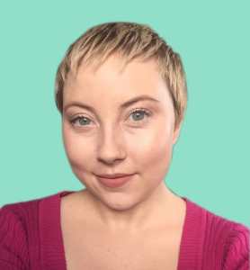 Photo of a woman with pale skin and and a short blonde pixie cut wearing a pink sweater with a teal background.