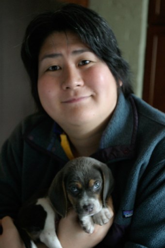 Image description: photo showing Karen Nakamura, an Asian woman holding a small grey beagle puppy — her service dog, Momo, who is now fully grown.