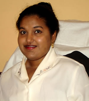 Young Indian American woman with black hair tied in a bun. She is wearing a cream colored shirt and gold earrings.