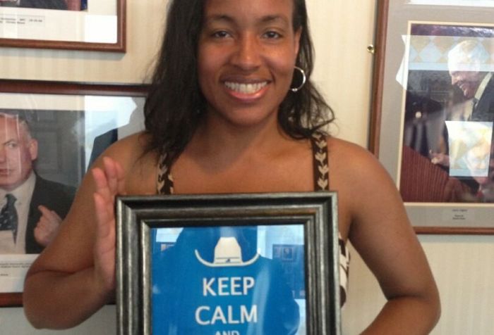 An African-American woman with long hair holding a framed poster that says 'Keep Calm and Lead On.' She is smiling at the camera.