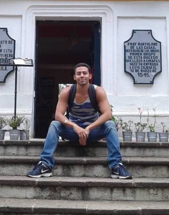 Krys, a Latinx person sitting on the front steps of a building, in Chiapas, Mexico in June 2015, while investigating Central American migration and security politics.