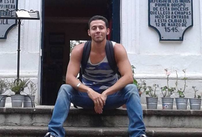 Krys, a Latinx person sitting on the front steps of a building, in Chiapas, Mexico in June 2015, while investigating Central American migration and security politics.