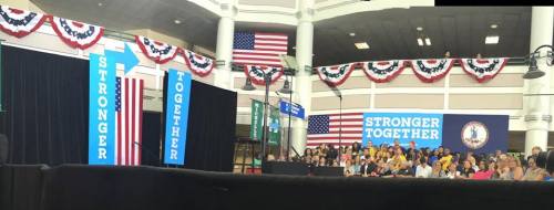 Photo of the stage at George Mason University that has a lectern and signs that say, "Stronger Together". Patriotic bunting and American flags are in the background.