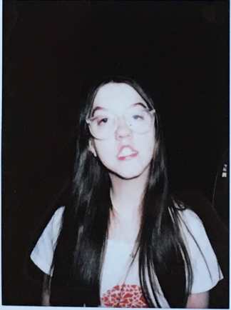 A young Caucasian woman with long dark hair, wearing clear glasses and a t-shirt with a design of a brain made out of red hearts on it.