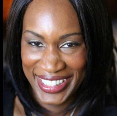A headshot of Morénike, a dark skinned Black person who is looking at the camera and smiling. Morénike has shoulder length black hair and is wearing a black shirt.