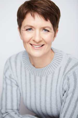 A headshot of Pia Justesen a white Danish woman with short brown hear and wearing a light blue sweater.