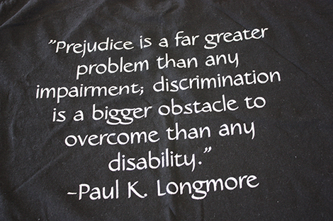 Dark fabric with a quote printed on it in white: "Prejudice is a far greater problem than any impairment; discrimination is a bigger obstacle to overcome than any disability." --Paul K. Longmore