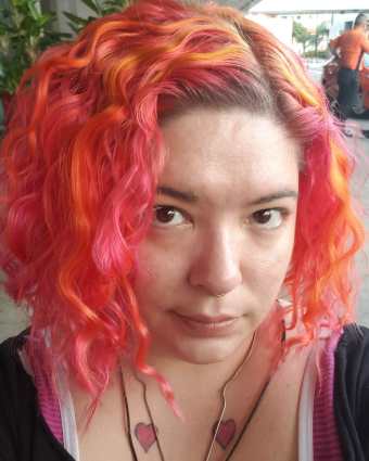 A photo headshot of a young woman with black hair smiling at the camera, wearing a white and plum colored plaid flannel shirt