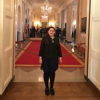 A woman standing against a red back drop behind The White House in the East Room.