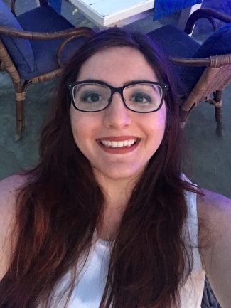 This image features a close up of a young woman's face. The woman is smiling, wearing a white shirt, and has long brown hair. 