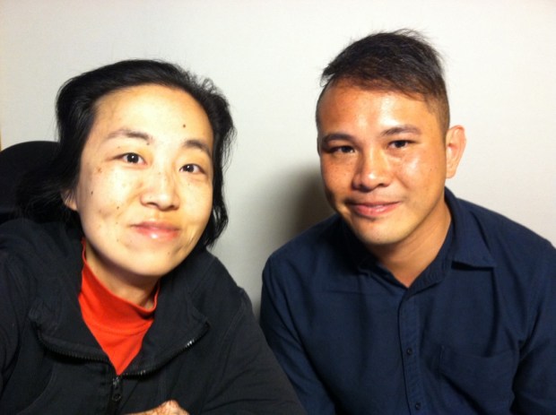 Photo of two Asian Americans. On the left is a middle-aged Asian American woman wearing a black hoodie and red turtleneck. On her right is a younger Asian American man with short hair and wearing a navy shirt.
