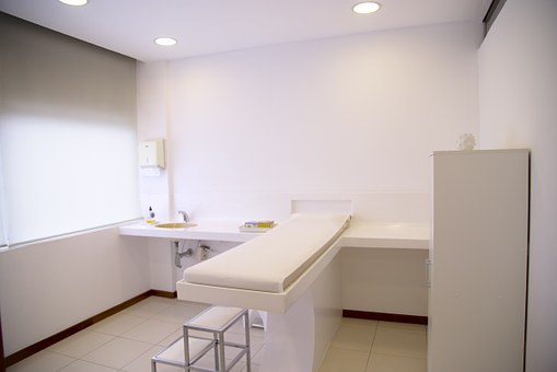 Image of an exam room that has everything in all white--white cabinets, countertops and an exam table with a small step stool.