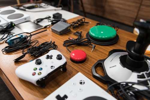 Photo courtesy of Microsoft. A table with the Xbox Adaptive Controller and an array of accessories such as a joystick, microswitch, foot pedal and other items. 