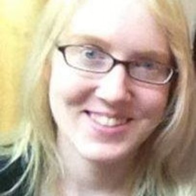 Picture of a young white woman with long blonde hair. She is smiling at the camera and wearing glasses.