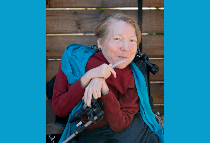 Graphic with a teal background. In the center a photo of Alana Theriault, a white woman, is sitting in a power wheelchair and smiling. She has short reddish-blonde hair that is beginning to gray. She is wearing a rust colored long sleeve shirt, a blue scarf, and gray slacks, and is holding a narrow clear ventilator tube in her hand. The background is a wooden fence. Photo Credit: DeAnna Tibbs Photography (deannatibbs.com) 