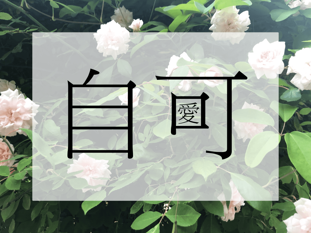 The Chinese character for self (自/zì) and the character in can (可/kě) with the traditional Chinese character for love (愛/ài) inside the character for mouth (口/ kǒu). The letters are black and are centred on a translucent white inset rectangular background in front of a background of an abundant bush of leaves and pink-white roses.