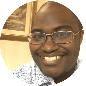 A black man wearing a button-down shirt and smiling.