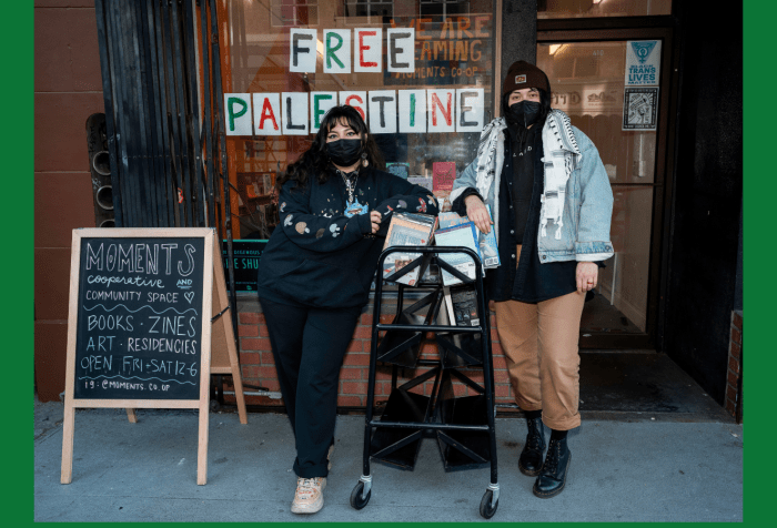 Graphic with a green background. In the center is a photo of Moments Cooperative and Community Space members Samantha and D posing outside the bookstore entrance wearing black KN95 masks. They are leaning against a cart of books for sale. Next to them is an A-Frame reading “Moments Cooperative and Community Space. Books. Zines. Art. Residencies. Open Fri-Sat 12-6. IG: @Moments.co.op.”Behind them in the window reads “FREE PALESTINE.” Photo by Brian Ringo, 2023.